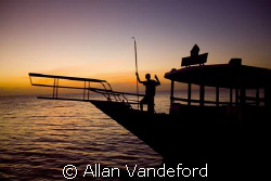 The staff returns a dive vessel at days end.  The sunset ... by Allan Vandeford 